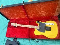 Yellow Telecaster-style electric guitar lying in yellow hardshell case with orange interior