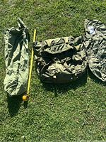 Photo showing the three items laid out on grass: nylon sleeping bag cover, large canvas field pack, and thinner canvas tote bag alongside a measuring tape.