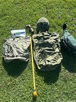 Full lot laid out on grass, showing waterproof nylon bag, white replacement cord, camouflage helmet, flashlight, and green waist pack with three water bottles.