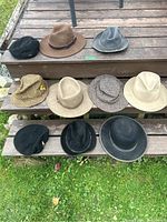 Photo showing 10 hats arranged on outdoor wooden steps with various colors and styles including fedoras, flattop caps, and bucket hats.