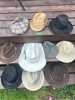 Top-side view of 10 assorted hats arranged on wooden steps, showing variety of colors and styles including fedoras, cowboy hat, bucket hat, and newsboy cap.