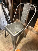 Side angled view of the metal chair showing curved backrest, embossed vertical panel, square seat with holes, and four legs.