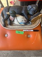 Image showing the black Labrador puppy lying next to the duck decoy and brown hunting boot on a textured base.
