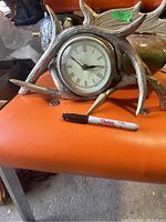 Antler style mantle clock displayed on orange chair with black Sharpie pen for scale.