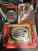 Three framed mirrored bar signs including Guinness Extra Stout, Gordon's Dry Gin, and Smith & Wesson, shown on plastic storage bin cover.