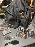 Photo of two black nylon motorcycle saddle bags by Sidewind with reflective strips, a Harley Davidson playing card tin, Harley Davidson cutting tool case, two motorcycle mirrors, and a flashlight in packaging.