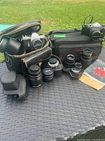 Overview of two cameras, multiple lenses, cases, bag and accessories on table outdoors