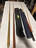 Top view showing three pool cues and two soft carrying cases on a white table.