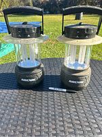 Two Rayovac outdoor lanterns placed on a black textured surface outdoors, showing front and side details. A sharpie marker is placed for scale.