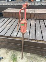 Front view of vintage red hand pump on steel pole showing overall condition and rust.