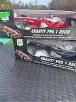 Two boxed Gravity Pro 1 Racer remote control cars, one red and white, one black and white, displayed on a dark table outdoors.