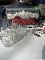 Coors illuminated beer sign with mountain design, front view taken in daylight showing white lit parts and cords visible
