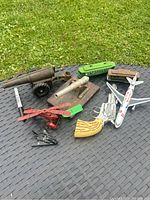 Photo showing overall lot including metal cast iron cannon, miniature metal cannon on wooden base, red and black metal model planes, green plastic toy train, two harmonicas, cowboy gun, and toy airplane.