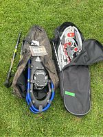 Two pairs of snowshoes with poles partially inside their carry cases on grass.