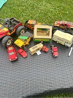 Group of vintage metal toy vehicles including camper trailers, trucks and a monster truck on black textured surface outdoors.