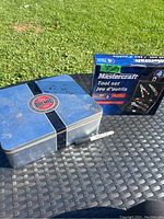 Rusty metal storage box with Dremel label on top, showing significant rust and wear on the surface, placed next to a Mastercraft 4-piece tool set box on an outdoor table.