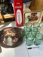 Photo shows six green Coca Cola glass mugs with handles, two round Pepsi Cola advertising trays, metal picnic tray, and red Coca Cola thermometer.