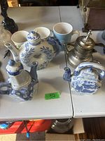 Overhead view of three blue and white stackable Chinese tea pots and three ceramic cups on a white table
