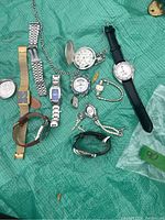 Wide view of all watches, pocket watch, bracelets, and pin on green cloth surface