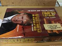 Photo of the board game box cover with Donald Trump's image and a note about hand-signed game booklet.