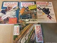 Four vintage Popular Mechanics magazines in a group, covers visible, featuring boating, home building, and automotive topics from the 1950s.