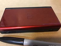 Closed Nintendo DS Lite console showing top cover in red glossy finish with DS logo.