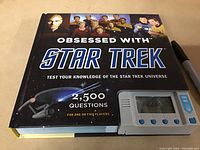 Front cover of the Star Trek trivia book showing title, Star Trek characters, USS Enterprise, and the attached digital game device with 'TRY ME' buttons.