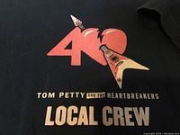 Close-up of the front chest design showing the red '40' graphic with heart and guitar. Text 'Tom Petty and the Heartbreakers Local Crew' below the graphic in cream lettering.