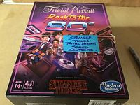 Top view of sealed Stranger Things Trivial Pursuit board game box with a bright 80s retro design and characters from the series.