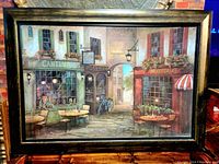 Front view of the framed lithograph depicting European-style courtyard scene with cafes and shops.