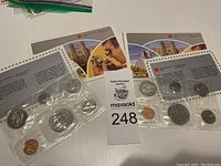 Two sealed 1986 Royal Canadian Mint uncirculated coin sets, each with seven coins including a large dollar coin, displayed alongside informational pamphlets.