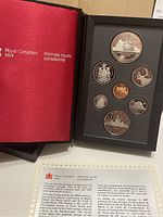 Open red booklet from the Royal Canadian Mint alongside the six proof coins set inside a black holder with coin indentations.