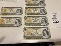 Top view of six 1973 Canadian one dollar bills laid out, showing all six bills and partial view of the table surface with auction card.