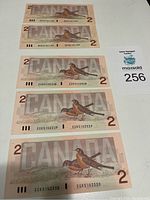 Five Canadian $2 banknotes with bird illustrations, three in sequential serial numbers and two in sequential serial numbers.