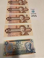 Front view of four Canadian $2 bills dated 1986, showing Queen Elizabeth II, arranged in a vertical row with a $5 bill at bottom.