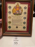 Front view of the framed nickel collection showing eleven coins arranged around a coat of arms and information sheet, highlighted by the wood frame and red matting.