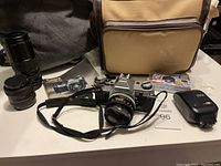 Overall view of camera, lenses, manual, bag, flash and film pack arranged on table