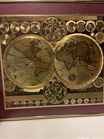 Full view of large vintage world map with gold foil detailing framed behind glass with a maroon mount and gold frame.