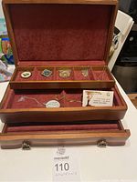 Open wooden jewelry box with red velvet interior showing 5 necklaces (4 with pendants), 1 single pendant, multiple decorative brooches, and a bracelet containing hearts.