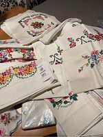 Various embroidered pillowcases showing floral cross-stitch work in multiple colors on white/cream linens.
