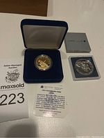 Two coins displayed with one in blue velvet case and another in plastic sleeve with displayed card and box.