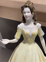 Close-up photo showing the upper body of the figurine, the facial features, and the details of the yellow off-shoulder dress.