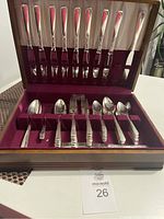 Open wooden case displaying stainless steel cutlery including knives, forks, and spoons with decorative handles.