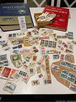 Two stamp albums (blue Statesman Deluxe, red The New Traveler Album) with loose stamps spread on table