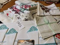 Tablecloths and napkins stacked showing embroidery, lace, and folded napkins with crocheted edges.