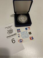 Silver coin in protective capsule resting in a blue velvet box with authenticity certificate and auction lot card.