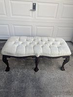 Full view of cream upholstered bench showing tufted fabric and carved dark wooden legs.