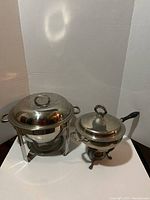 Photo showing side-by-side the 5Qt round stainless steel chafing dish with lid and stand, and the smaller 2Qt round chafing dish with metal stand and burner.