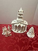 Eight piece white porcelain Christmas set displayed including church, Christmas tree with small chip, and six figurines grouped together.