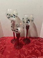Three Pfaltzgraff Winterberry glass candleholders with painted holly berries visible upright on red stems.